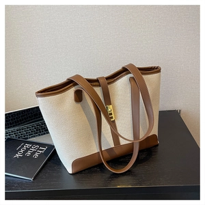 Detail of canvas tote bag with brown leather trim and golden metal clasp on desk