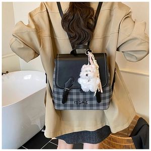 Close-up of stylish backpack with checkered fabric, leather trim, and a cute dog charm