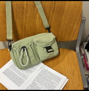 Detail of sage green nylon crossbody bag with dual functional pockets and clip buckles