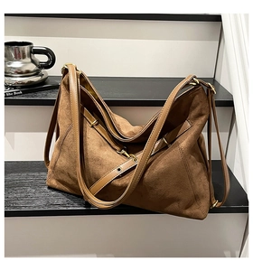 Close-up of brown frosted leather tote bag with vintage gold buckles on black shelf