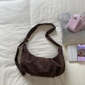 Detail of dark brown suede crescent bag with wide knotted strap on a soft white fabric