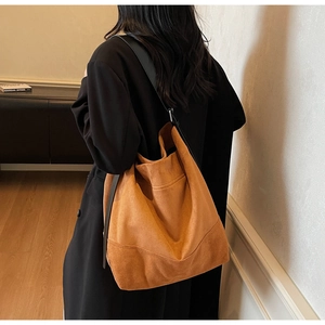 Detail of caramel suede tote bag with black shoulder strap worn in a minimalist interior
