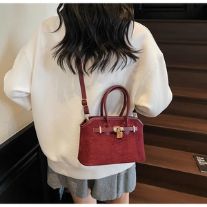 Détail du sac coquille rouge foncé mat avec cadenas doré sur un escalier en bois