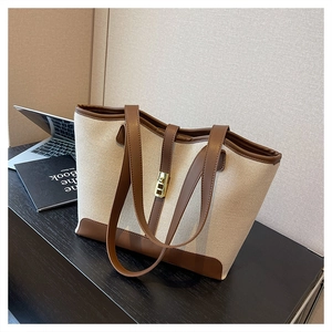 Detail of canvas tote bag with brown leather trim and golden metal twist-lock closure