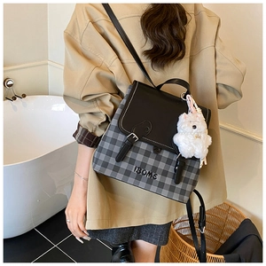 Detail of checkered backpack with leather flap and plush bear charm on a female model