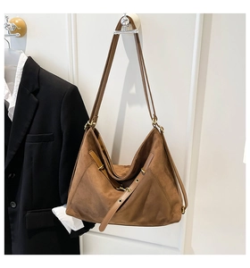 Brown faux suede tote bag with long strap and gold buckle hanging on a wall