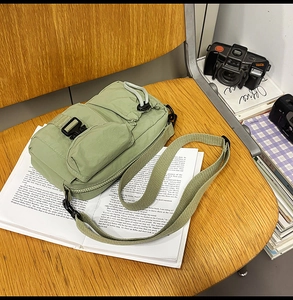 Detail of light green nylon crossbody bag with multi-pockets and buckle on wooden chair