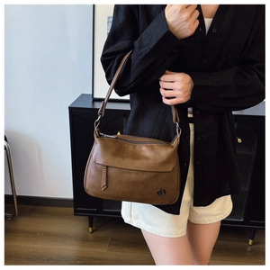 Close-up of vintage brown leather square bag with tassel and metal logo on strap
