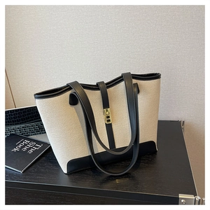 Detail of canvas tote bag with black leather trim and gold twist lock on wooden desk