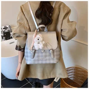 Detail view of grey plaid backpack with leather strap buckle and cute plush dog pendant