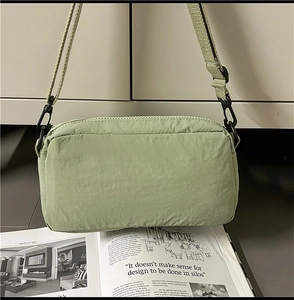 Detail of mint green nylon crossbody bag with black zipper and wide fabric strap