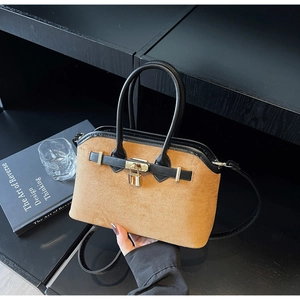 Détail du sac coquille en daim avec poignées en cuir et cadenas doré sur bois noir