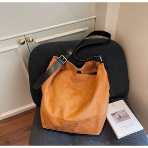Detail of caramel suede tote bag with black leather strap on a blue velvet chair