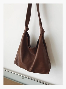 Detail of dark brown hobo bag showing litchi leather texture and decorative shoulder knots