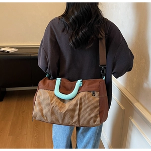 Model showing large brown patchwork travel bag with light blue handles and shoulder strap