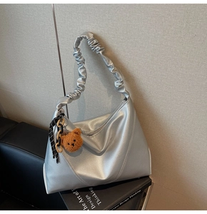 Détail d'un sac argenté en cuir grainé avec poignée plissée et breloque ourson