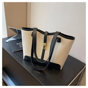 Close-up of beige canvas tote bag featuring black leather trim and golden metal buckle