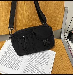 Detail of black nylon crossbody bag with utility pockets and buckle on wooden seat