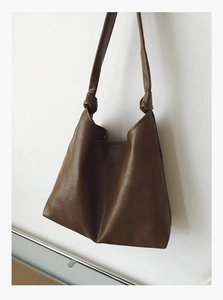 Detail of a brown PU leather tote bag showing a knotted shoulder strap and fine texture