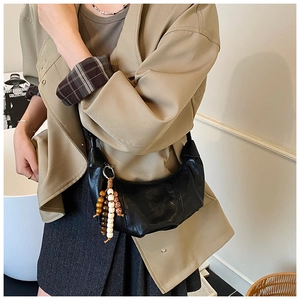 Detail of black croissant shoulder bag with colorful wooden bead charm on a beige trench coat
