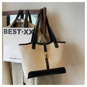 Detail of canvas tote bag with black leather trim and golden rectangular metal twist lock