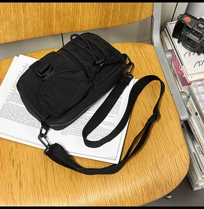 Detail of black nylon functional crossbody bag with multiple pockets on a wooden chair