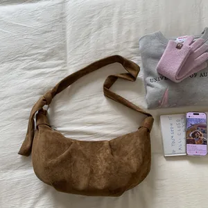 Detailed view of brown suede dumpling bag with wide knot-style shoulder strap detail