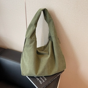 Sac hobo vert herbe en velours côtelé avec forme demi-lune sur un canapé en cuir noir