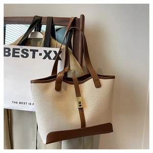 Detail of canvas tote bag with brown leather trim and golden metal clasp on a wooden hanger