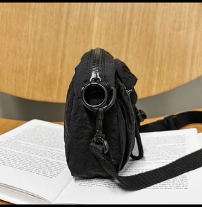 Detail of black crossbody bag side with metal zipper and ring on a vintage book background