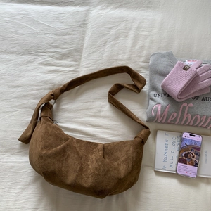 Detailed close-up of dark brown suede dumpling bag with unique knot shoulder strap detail