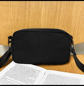 Close-up of black crossbody bag with textured fabric resting on a vintage book