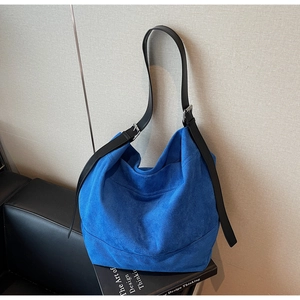 Blue suede hobo bag shown on a leather sofa next to a book for a lifestyle detail shot