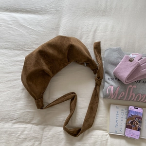 Detail of a brown suede half-moon crossbody bag with a knotted shoulder strap design