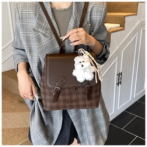 Detail of checkered brown backpack with plush puppy charm and vintage buckle closure