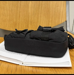 Detail view of black nylon crossbody bag with functional multi-pockets on a book