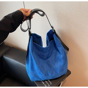 Close-up of blue suede tote bag featuring a black wide leather strap and silver buckle