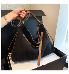 Detail of black canvas tote bag showing brown leather strap and gold metal buckles