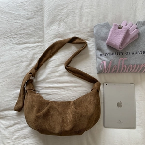 Detailed view of brown suede dumpling bag with decorative knot strap on a white bed
