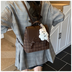 Close-up of vintage brown plaid backpack with leather straps and white dog plush pendant