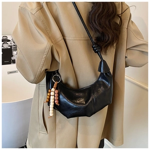 Detail of black glossy croissant bag with ruched texture and wooden bead charm on strap