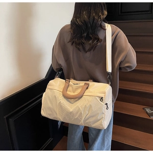 Detail of a large beige sports gym bag with brown handles on wooden stairs in a warm setting