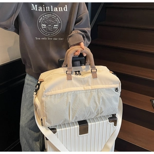 Travel bag with back sleeve sliding over the handle of a white wheeled suitcase