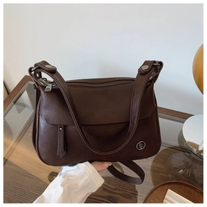 Close-up of dark brown leather texture and metal logo on a vintage crossbody bag