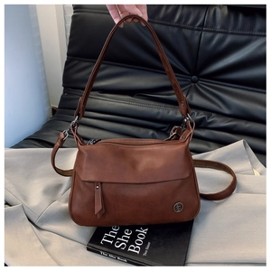 Detailed view of a vintage brown leather crossbody bag with metallic logo and top handle