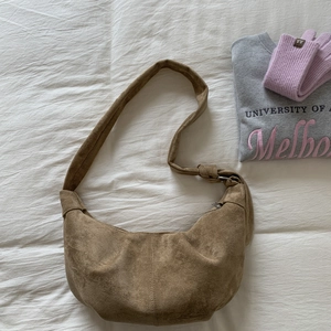 Close-up of brown suede crescent bag with knot detail on white fabric background