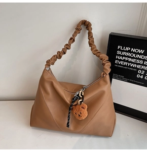 Détail du sac hobo en cuir marron avec bandoulière froncée et breloque ours en peluche