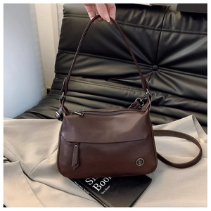 Detail of dark brown leather handbag featuring a round metal logo and zipper closure
