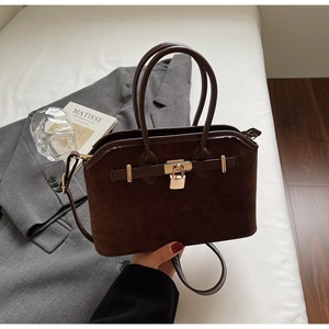 Détail du sac coquille en daim marron foncé avec fermoir doré et bandoulière sur lin