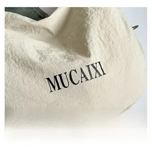 Détail macro montrant la texture plissée unique du tissu et le logo MUCAIXI noir du sac